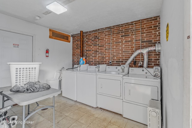 laundry area with brick wall, independent washer and dryer, light tile floors, and radiator