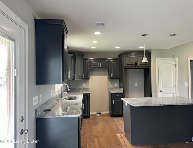 kitchen with sink, light hardwood / wood-style floors, decorative light fixtures, a kitchen island, and light stone countertops