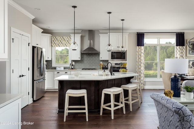 kitchen with a center island with sink, stainless steel appliances, wall chimney range hood, tasteful backsplash, and decorative light fixtures