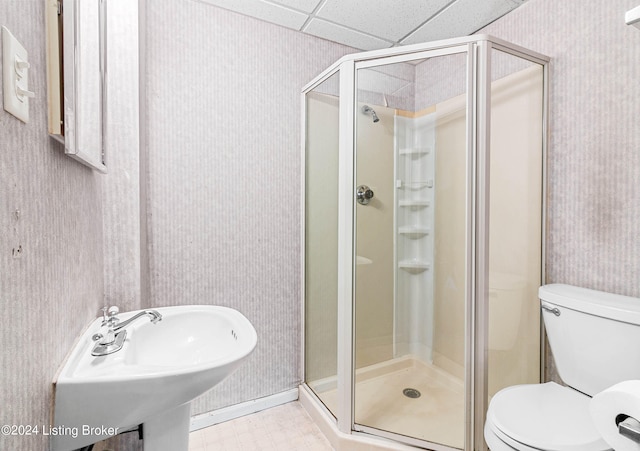 bathroom featuring a drop ceiling, walk in shower, toilet, sink, and tile floors