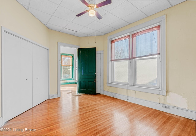 unfurnished bedroom featuring a closet, ceiling fan, a drop ceiling, and light hardwood / wood-style flooring