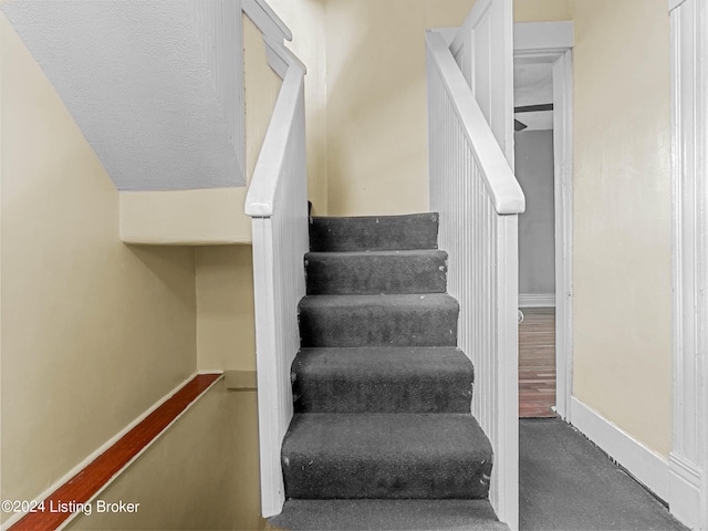 stairway featuring lofted ceiling and dark carpet