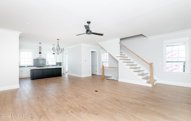 unfurnished living room with sink, crown molding, light wood-type flooring, and ceiling fan with notable chandelier