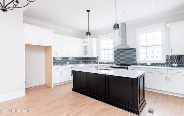 kitchen featuring a center island with sink, tasteful backsplash, light wood-type flooring, and wall chimney range hood