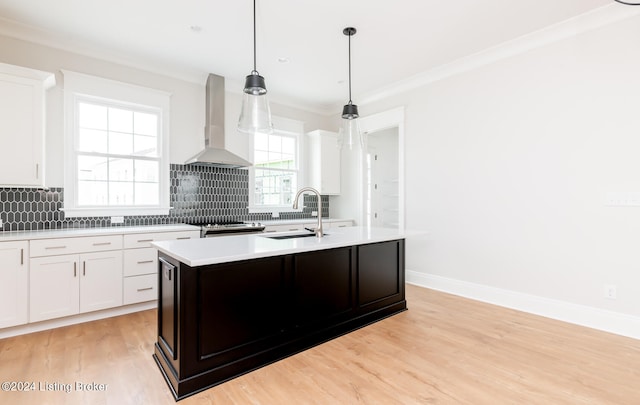 kitchen with wall chimney range hood, light wood-type flooring, tasteful backsplash, and a center island with sink