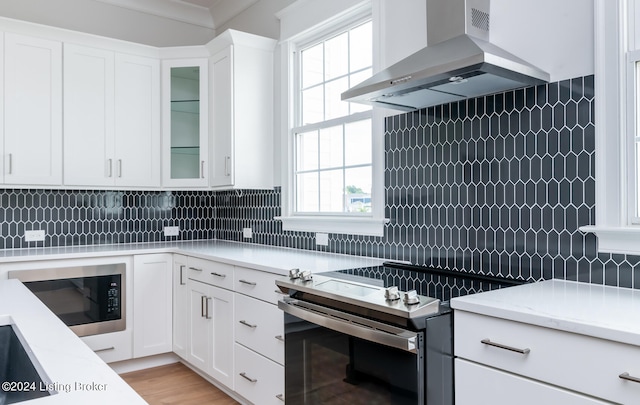 kitchen with wall chimney range hood, backsplash, and a wealth of natural light