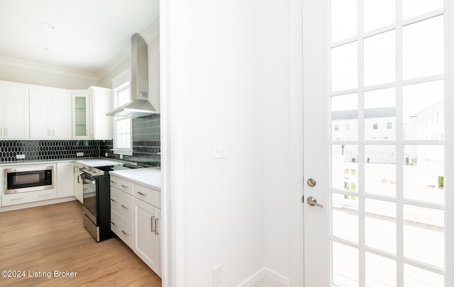 kitchen featuring wall chimney range hood, stainless steel range with electric cooktop, black microwave, light hardwood / wood-style flooring, and backsplash