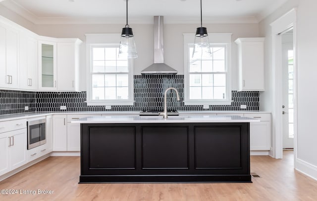 kitchen featuring light hardwood / wood-style flooring, tasteful backsplash, white cabinets, stainless steel microwave, and wall chimney exhaust hood