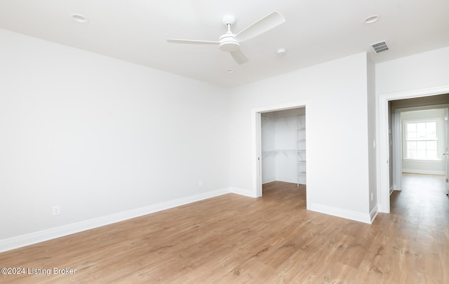 unfurnished bedroom featuring a spacious closet, a closet, light wood-type flooring, and ceiling fan