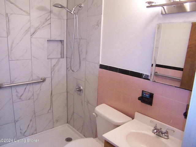 bathroom featuring a tile shower, tasteful backsplash, toilet, vanity, and tile walls