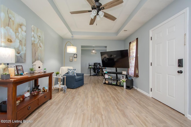 living area with light wood-style flooring, a raised ceiling, baseboards, and a ceiling fan