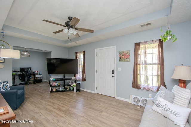living area with ceiling fan, visible vents, wood finished floors, and a raised ceiling