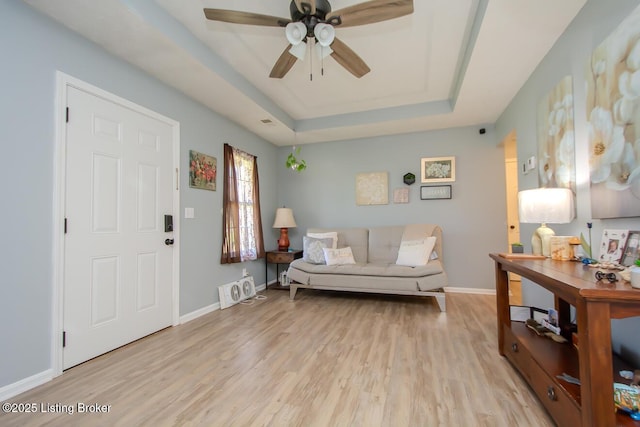 living room featuring a tray ceiling, light wood-style floors, ceiling fan, and baseboards