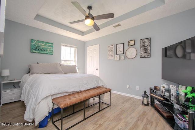 bedroom with a raised ceiling, wood finished floors, baseboards, and visible vents