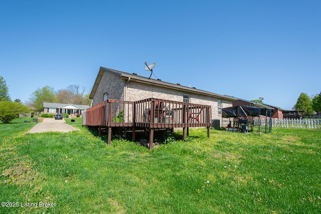 back of property with brick siding, fence, a deck, and a yard