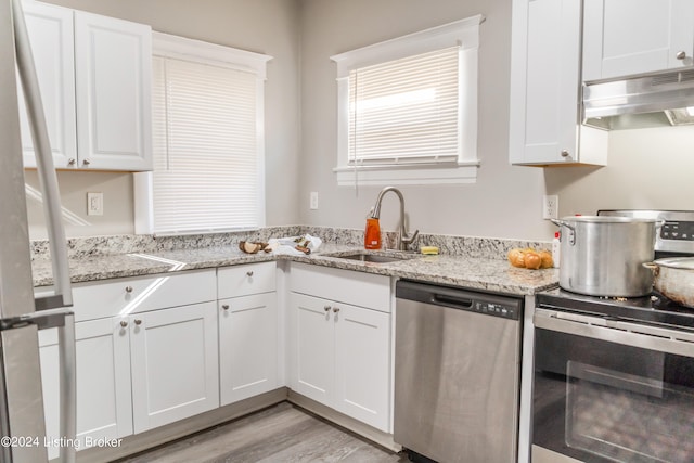 kitchen featuring sink, stainless steel appliances, wall chimney range hood, white cabinetry, and light wood-type flooring