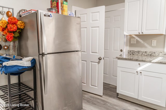 kitchen with light stone counters, stainless steel refrigerator, white cabinetry, and light hardwood / wood-style flooring