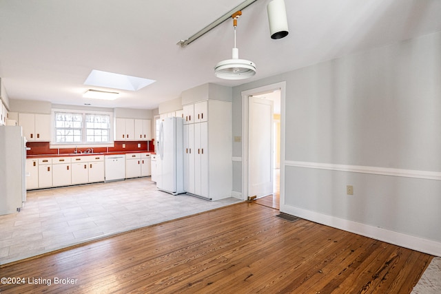 kitchen featuring a skylight, white cabinetry, white appliances, sink, and light tile floors