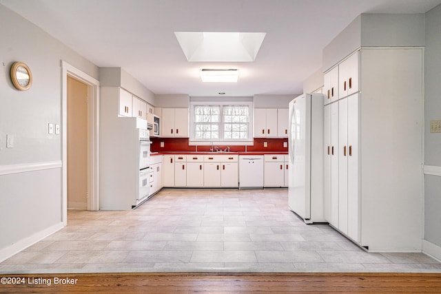 kitchen with a skylight, white cabinets, light tile floors, white appliances, and sink