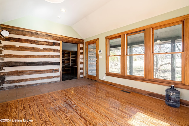 unfurnished living room featuring dark tile flooring, vaulted ceiling, and a healthy amount of sunlight