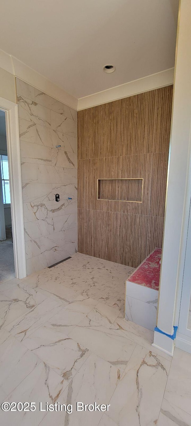 bathroom featuring stone wall, marble finish floor, and ornamental molding