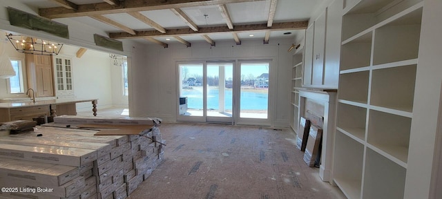 interior space featuring a water view, an inviting chandelier, beam ceiling, a fireplace, and a sink