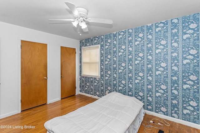 bedroom with light hardwood / wood-style floors, ceiling fan, and multiple closets