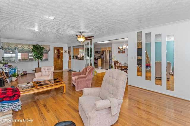 living room featuring crown molding, a textured ceiling, ceiling fan with notable chandelier, and light hardwood / wood-style flooring