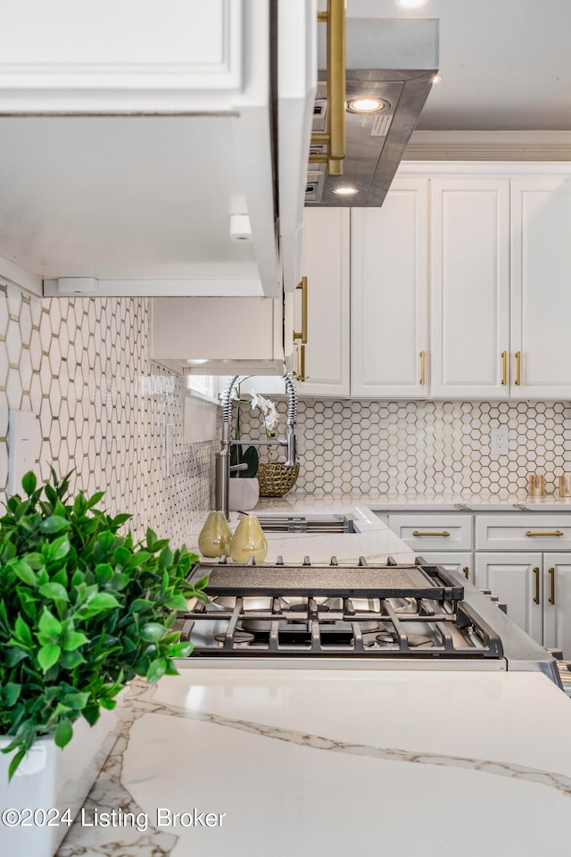 kitchen with backsplash, ventilation hood, white cabinets, and light stone counters