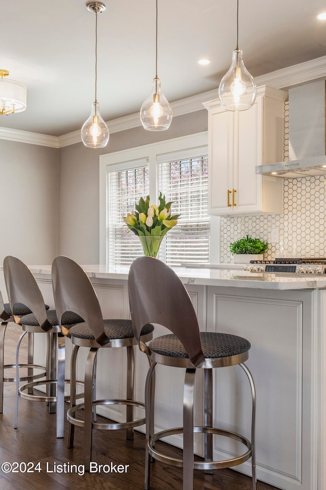 interior space featuring dark hardwood / wood-style floors, white cabinets, wall chimney range hood, tasteful backsplash, and a kitchen bar