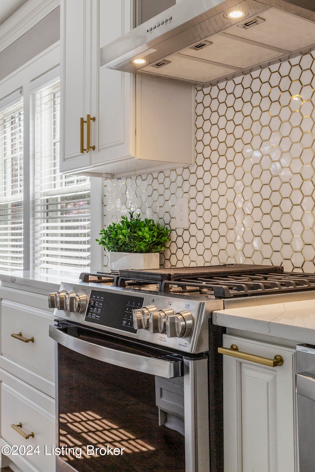 kitchen with backsplash, fume extractor, stainless steel range, and white cabinetry