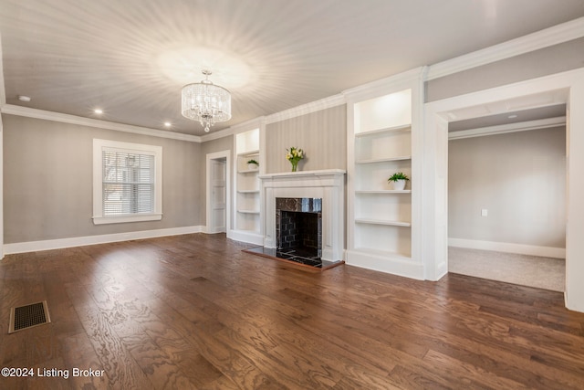 unfurnished living room featuring built in shelves, crown molding, a tiled fireplace, dark wood-type flooring, and an inviting chandelier