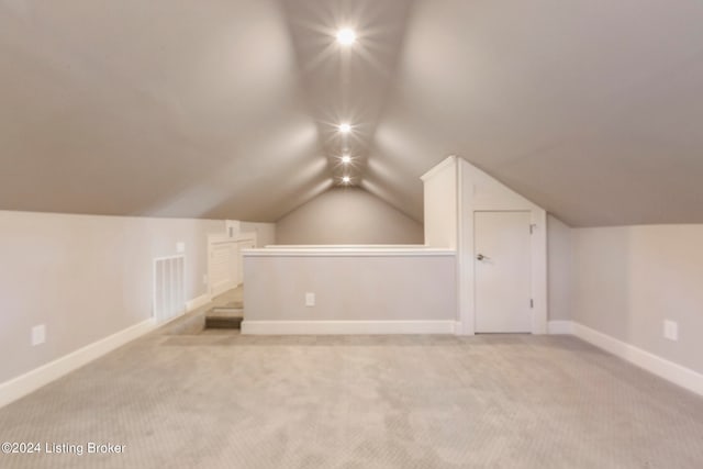 additional living space featuring light colored carpet and vaulted ceiling