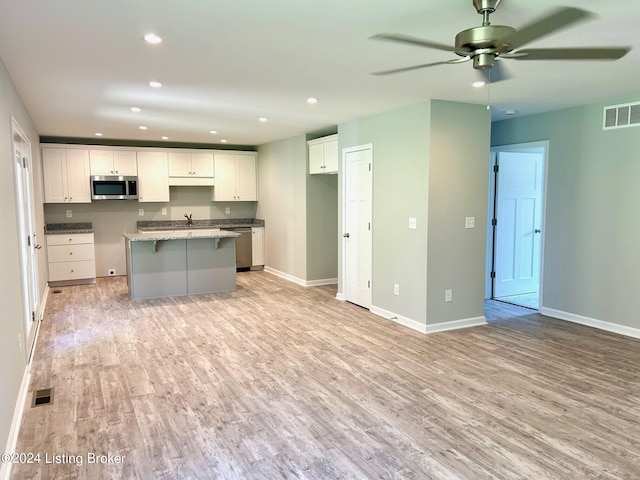 kitchen featuring light hardwood / wood-style flooring, white cabinetry, light stone countertops, an island with sink, and stainless steel appliances