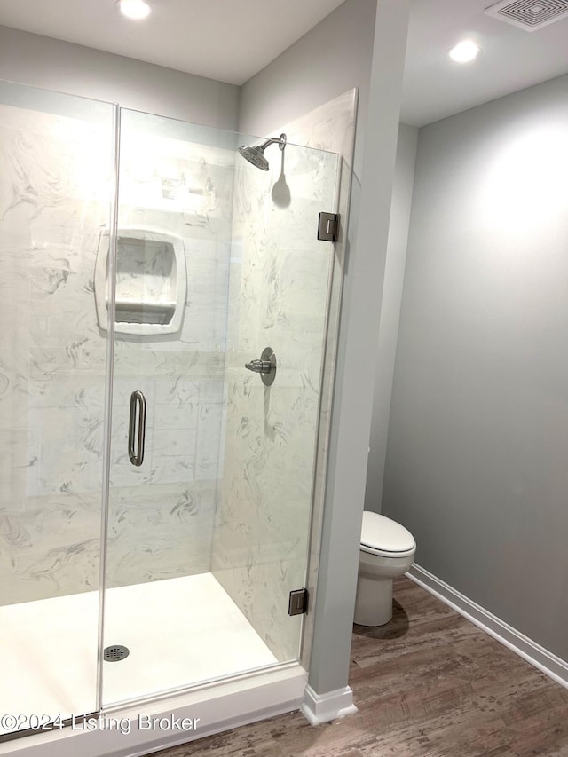 bathroom featuring hardwood / wood-style floors, toilet, and a shower with door