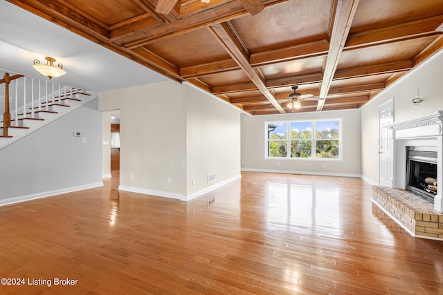 unfurnished living room featuring beamed ceiling, ceiling fan, a fireplace, coffered ceiling, and light hardwood / wood-style floors