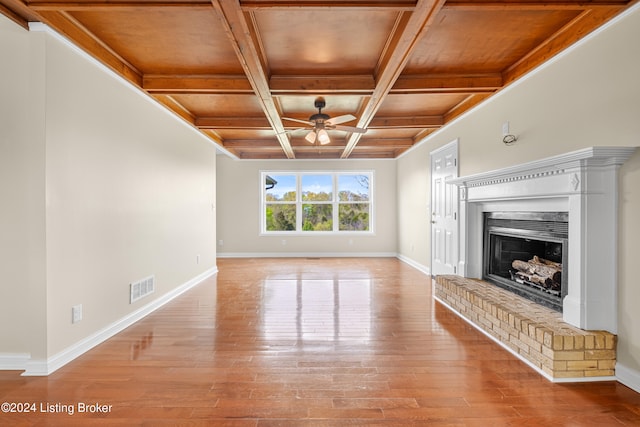 unfurnished living room with beamed ceiling, ceiling fan, a fireplace, coffered ceiling, and light wood-type flooring