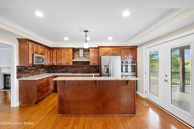 kitchen featuring wall chimney exhaust hood, a kitchen island, tasteful backsplash, stainless steel appliances, and wood-type flooring