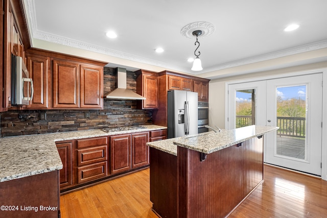 kitchen featuring stainless steel appliances, light hardwood / wood-style floors, tasteful backsplash, wall chimney range hood, and pendant lighting