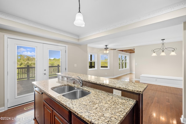 kitchen with light stone countertops, sink, decorative light fixtures, a kitchen island with sink, and hardwood / wood-style floors