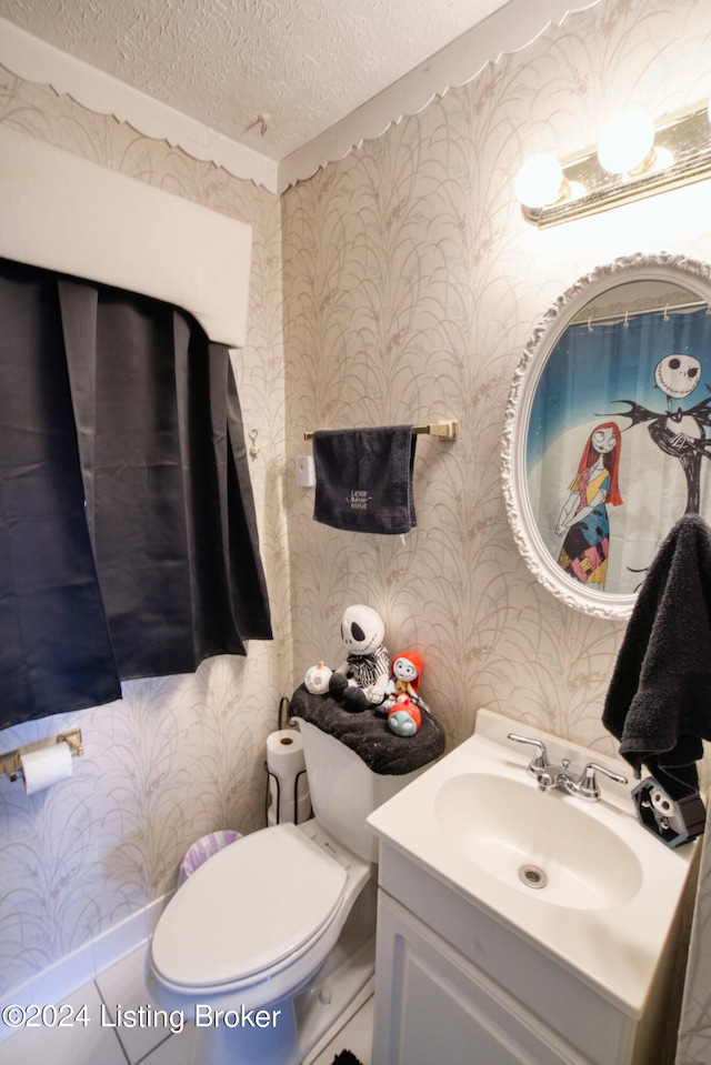 bathroom with wallpapered walls, vanity, toilet, and a textured ceiling