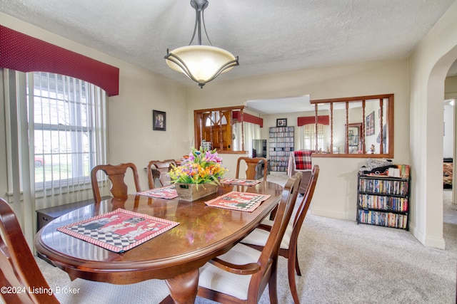 carpeted dining room with arched walkways, baseboards, and a textured ceiling