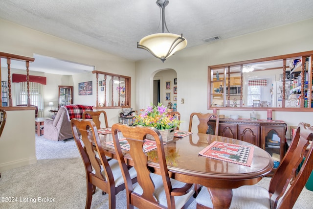 dining area featuring light colored carpet, visible vents, a textured ceiling, and arched walkways