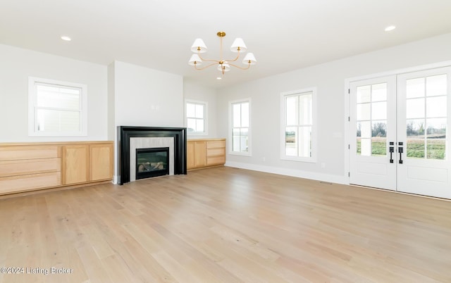 unfurnished living room featuring a notable chandelier, light hardwood / wood-style floors, and french doors