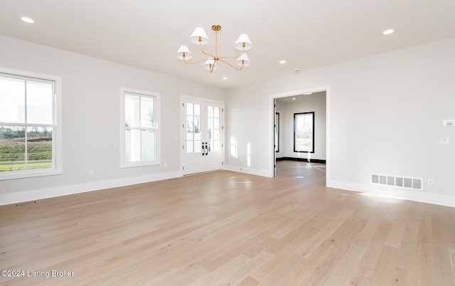 empty room with an inviting chandelier, french doors, and light hardwood / wood-style flooring