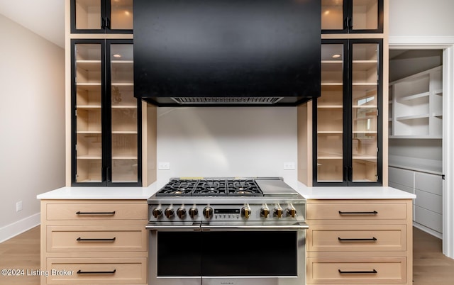 kitchen with extractor fan, cream cabinetry, light hardwood / wood-style flooring, and range with two ovens