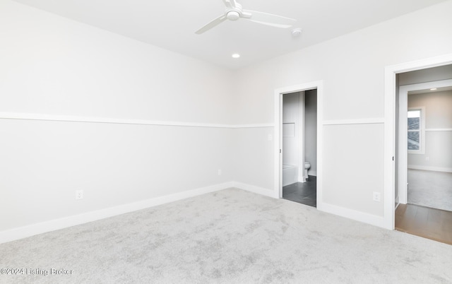 unfurnished bedroom featuring ensuite bathroom, dark carpet, and ceiling fan