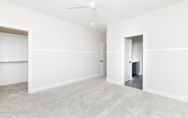 unfurnished bedroom with a spacious closet, dark carpet, and ceiling fan