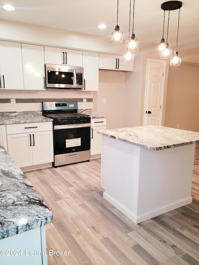 kitchen with appliances with stainless steel finishes, hanging light fixtures, white cabinetry, and a center island