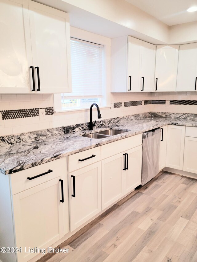 kitchen featuring sink, white cabinets, light hardwood / wood-style flooring, light stone countertops, and stainless steel dishwasher